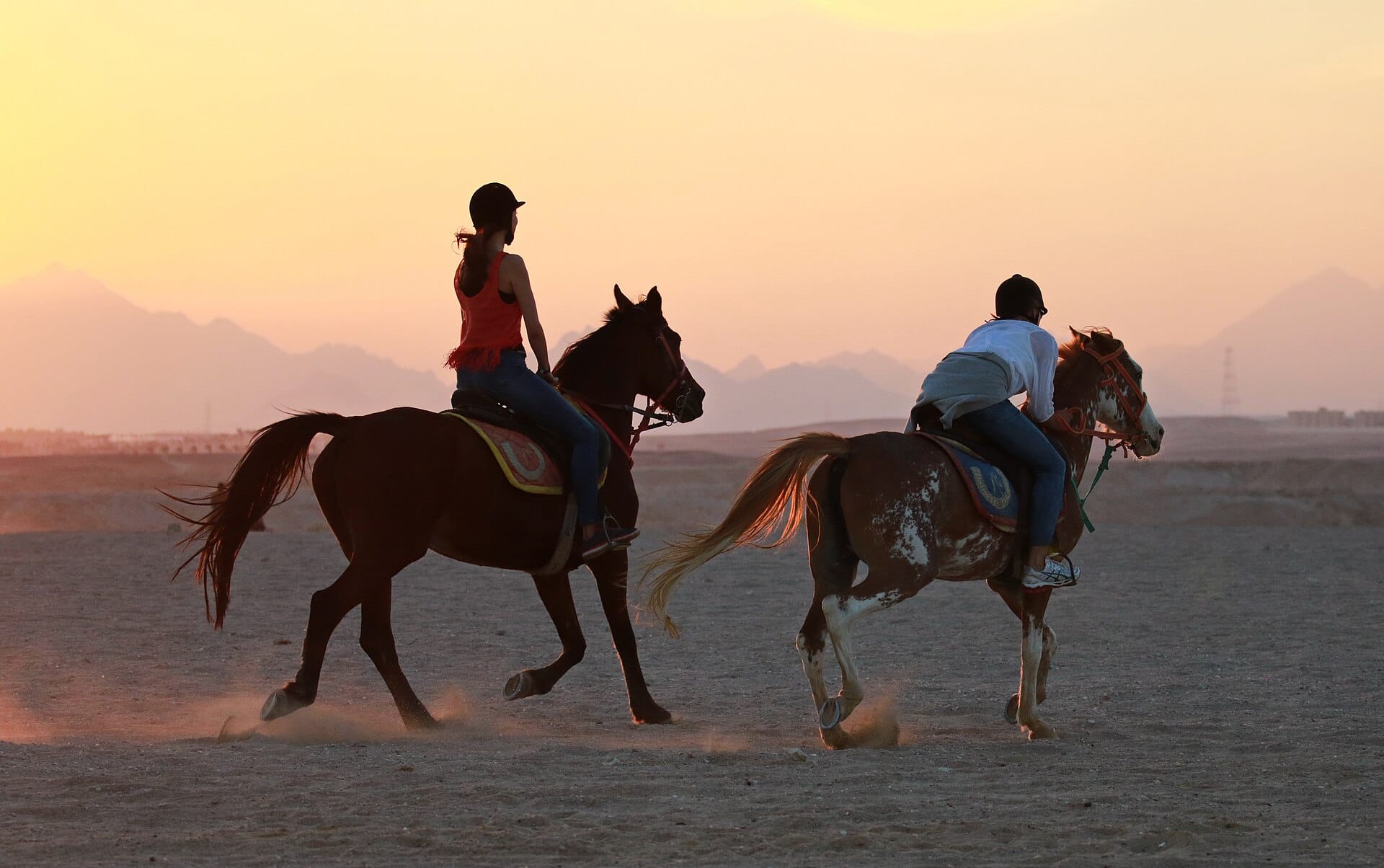 Riders cantering across the sand at dusk